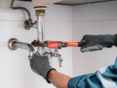 Plumber using a wrench to repair water pipe under the sink. Plumber using a wrench to repair water pipe under the sink.